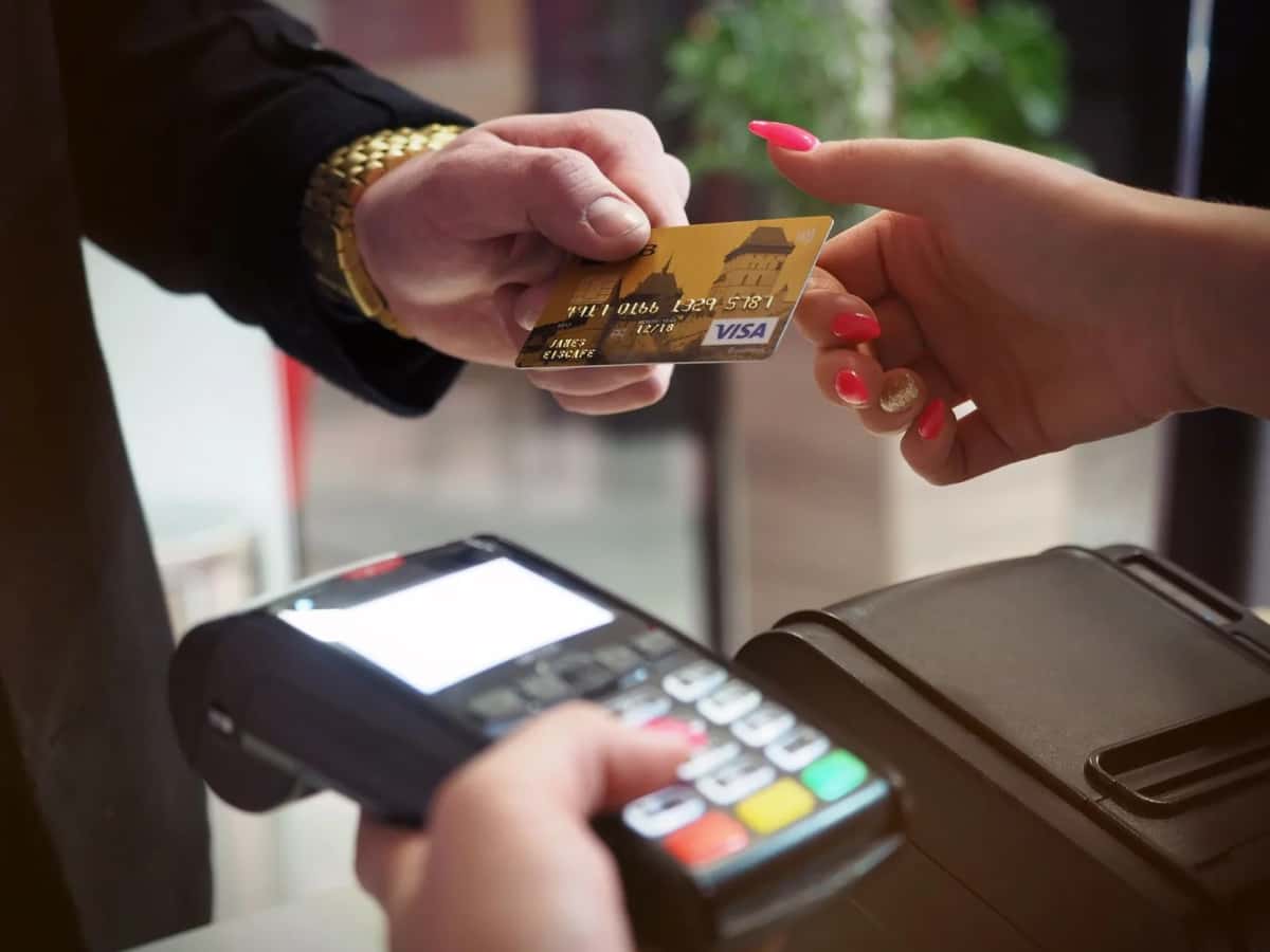 Une carte bancaire tendue au-dessus d'un terminal de paiement, deux mains se faisant face