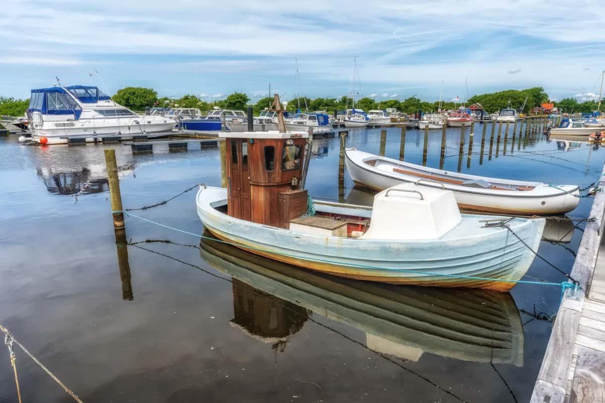 Vieux bateau de pêche en bois amarré dans un petit port de plaisance, devant des pontons et des cabanes rouges