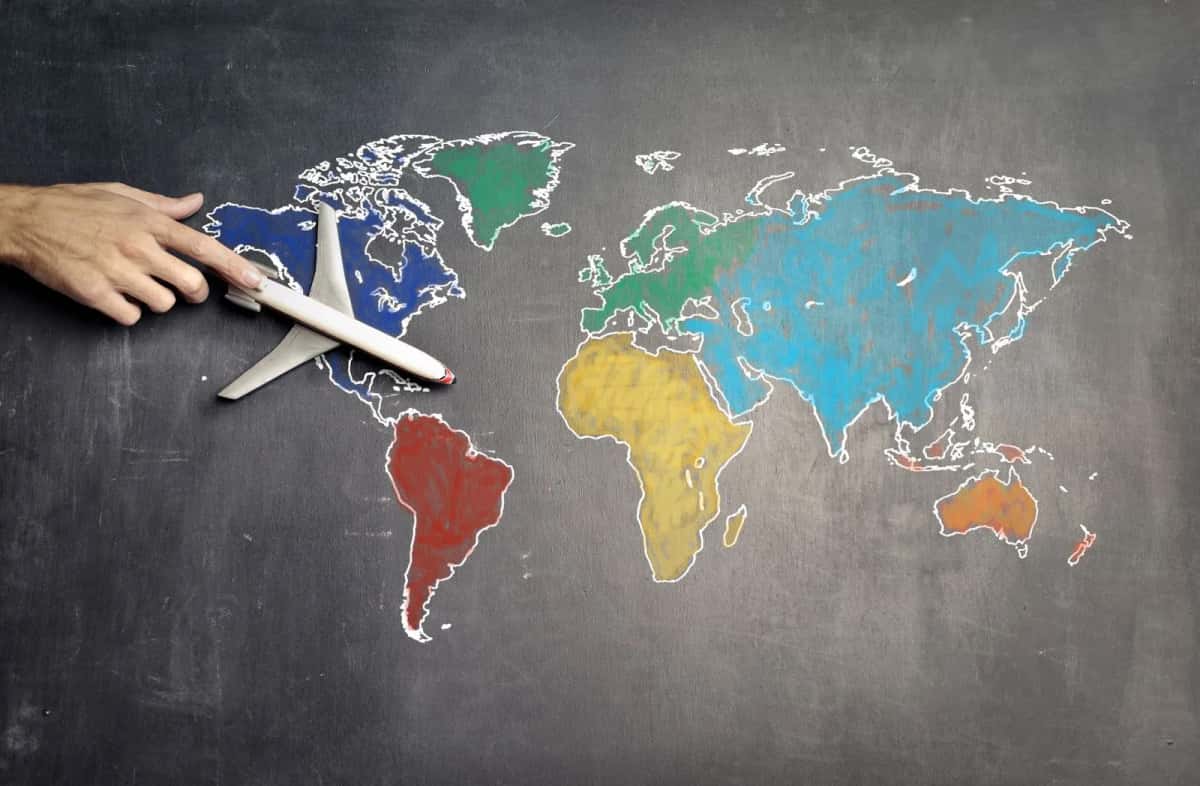 Petit avion en bois posé sur une carte du monde dessinée à la craie sur un tableau noir, une main le faisant avancer