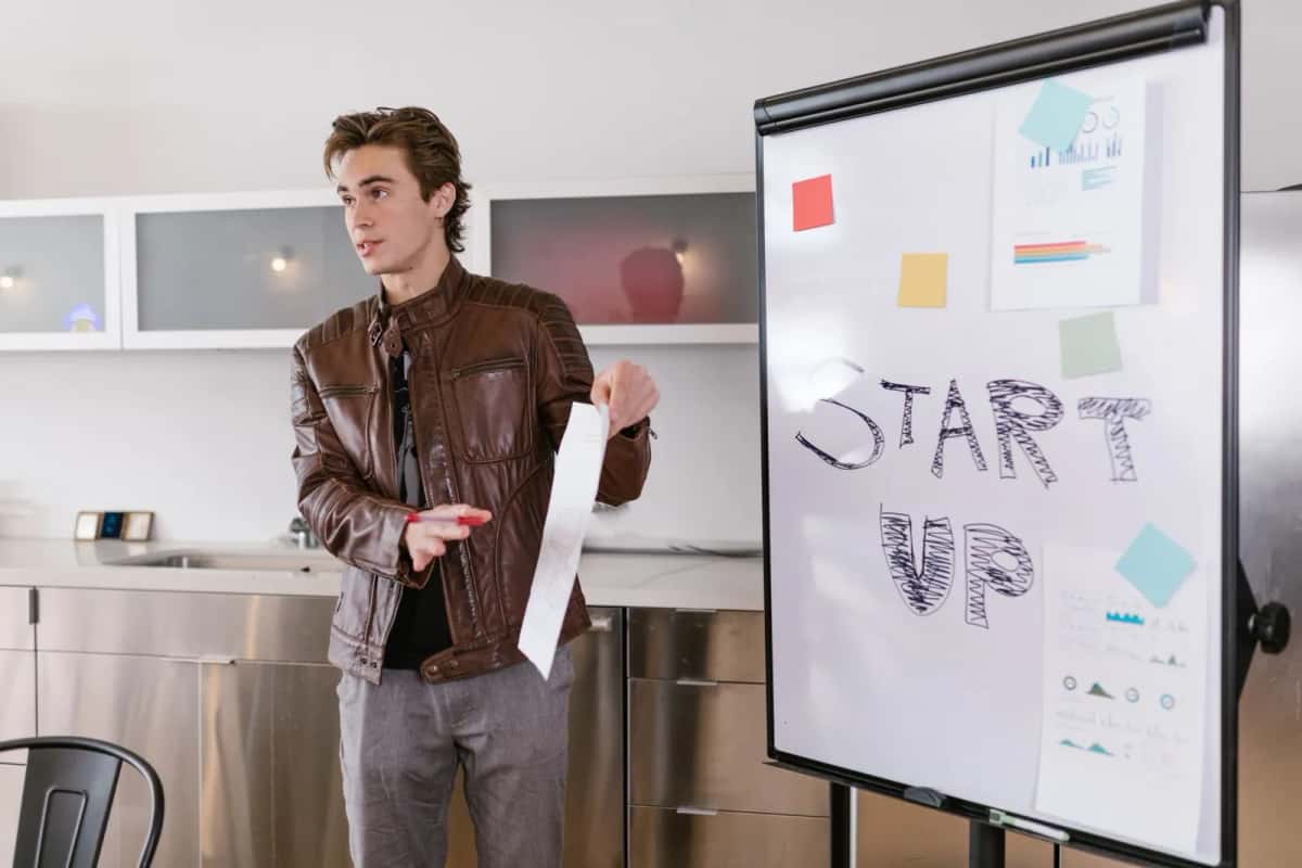Un homme présentant un projet devant un paperboard portant le mot « start up » et des notes autocollantes de couleur