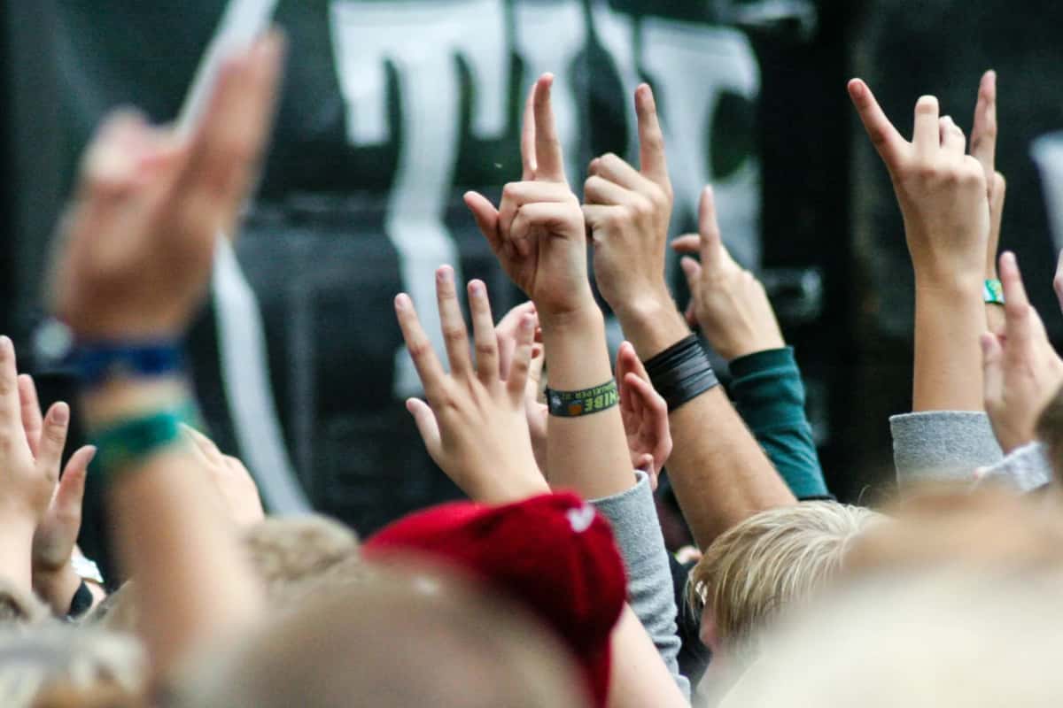 Mains levées dans le public d'un concert en plein air, bracelets de festival danois aux poignets, scène sombre et floue en arrière-plan