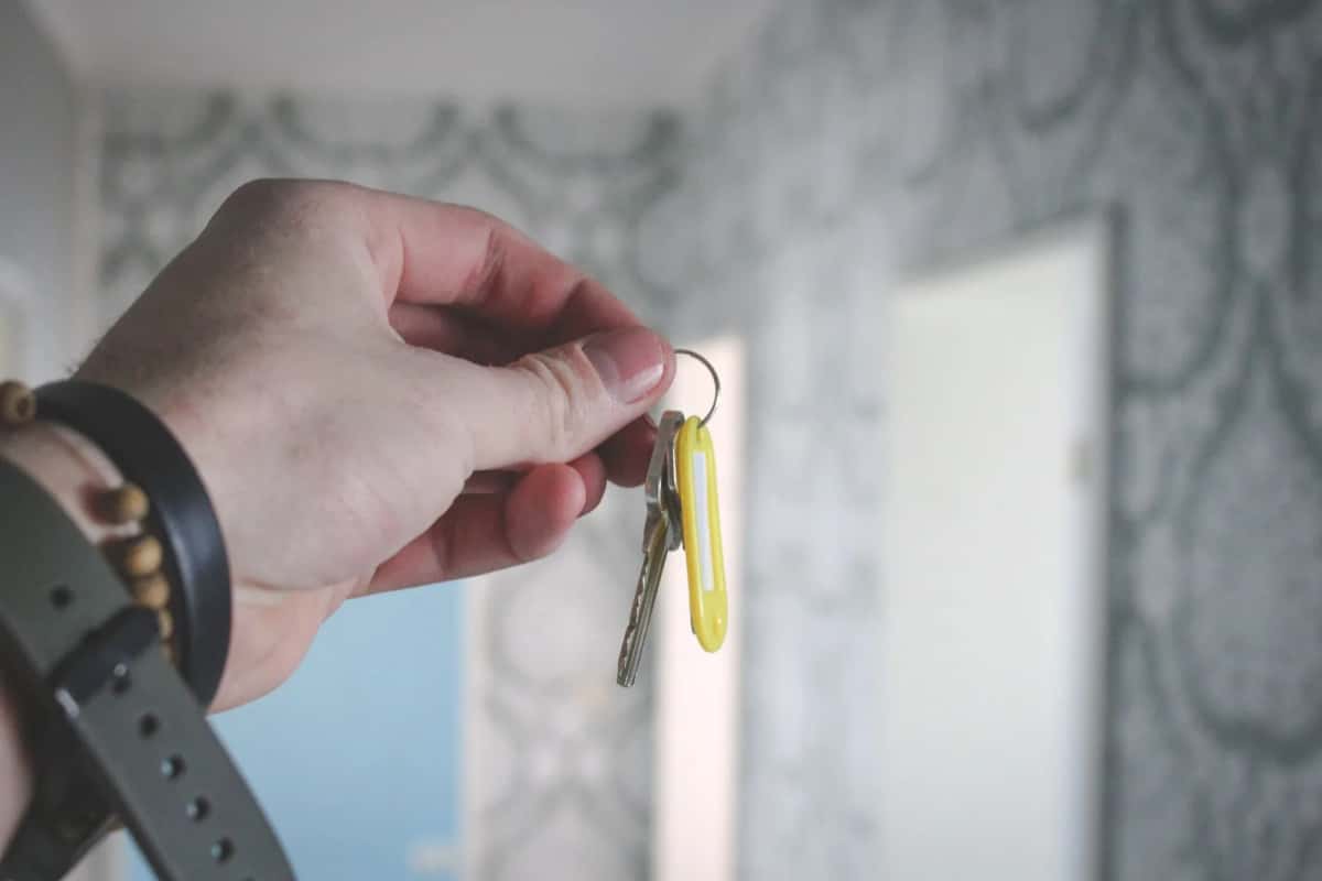 Une main tend un trousseau de deux clés devant une porte blanche entrouverte
