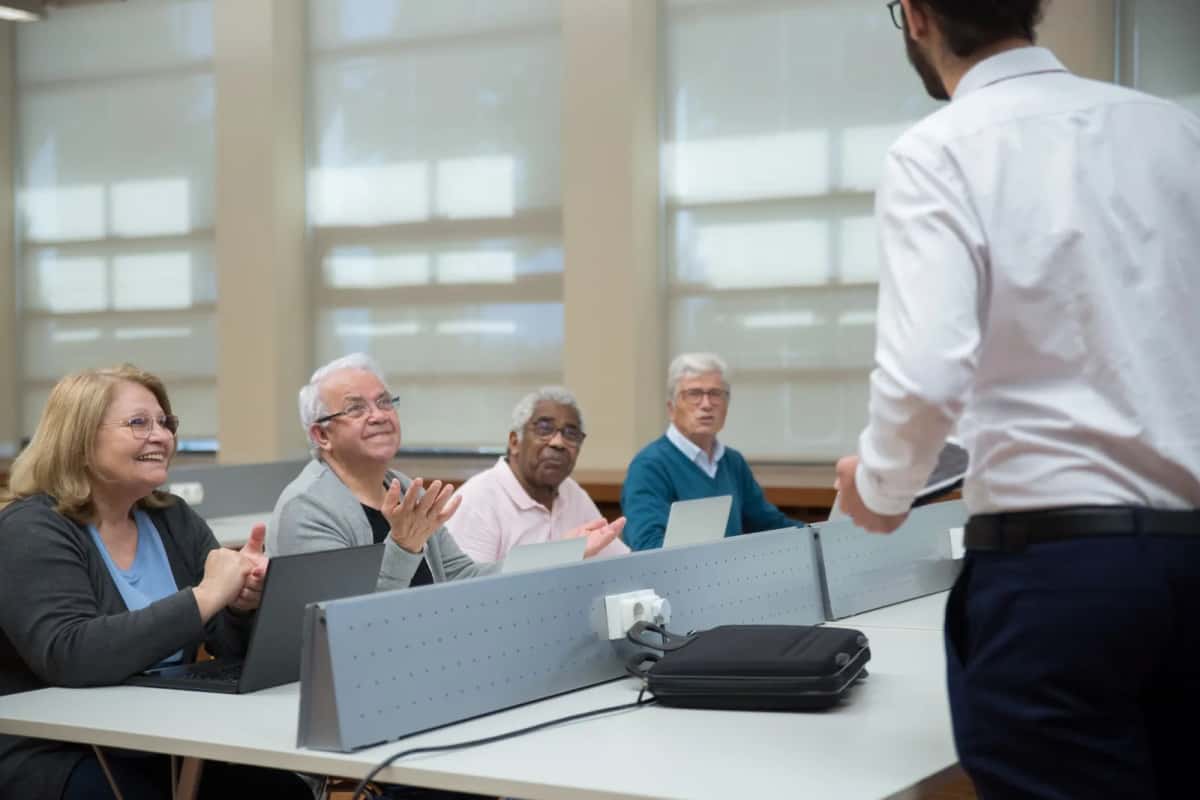 Public d'une dizaine d'adultes assis en salle, applaudissant un intervenant debout devant eux