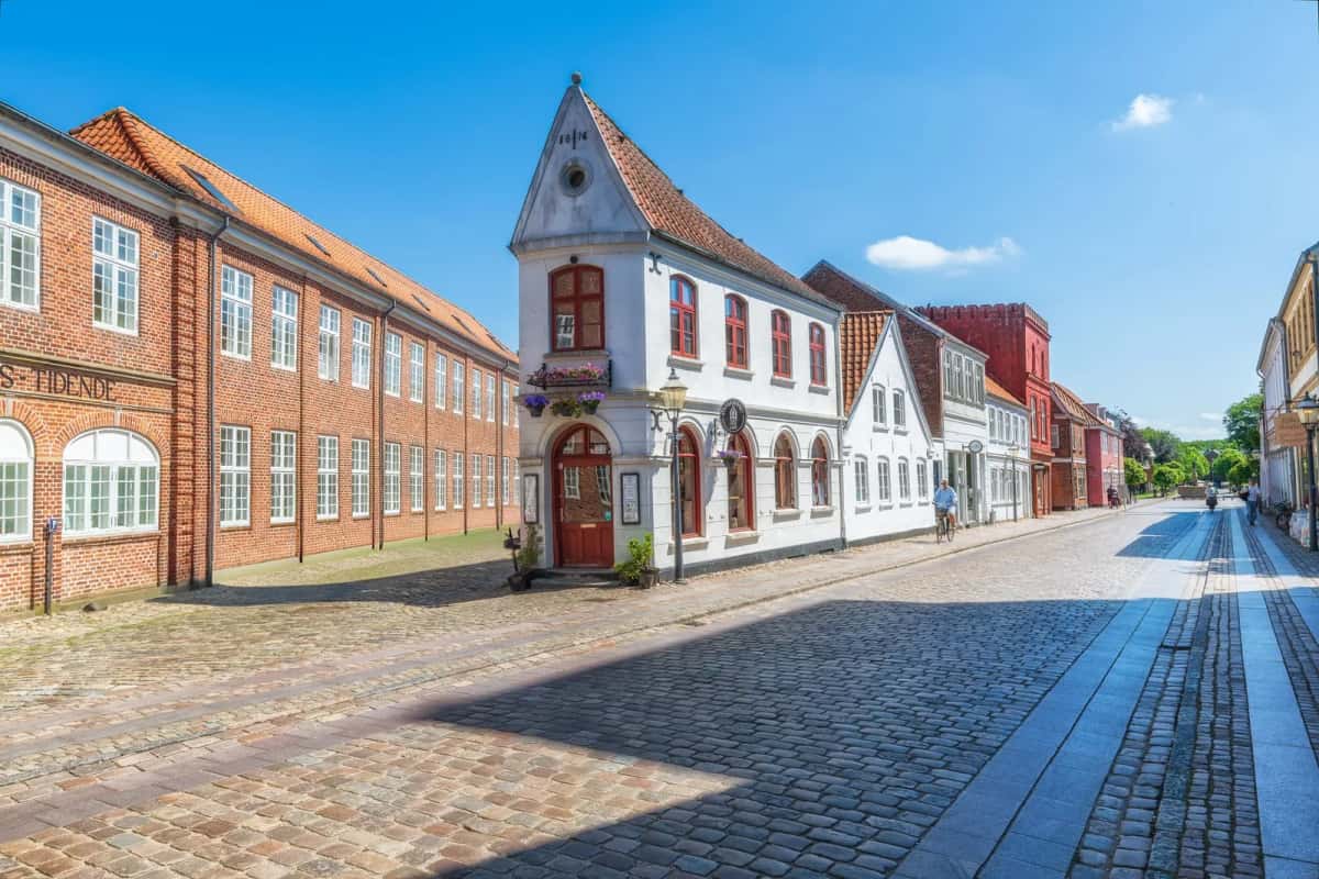 Rue pavée du centre historique de Ribe, plus ancienne ville du Danemark, bordée de maisons à colombages sous un ciel bleu, Jutland