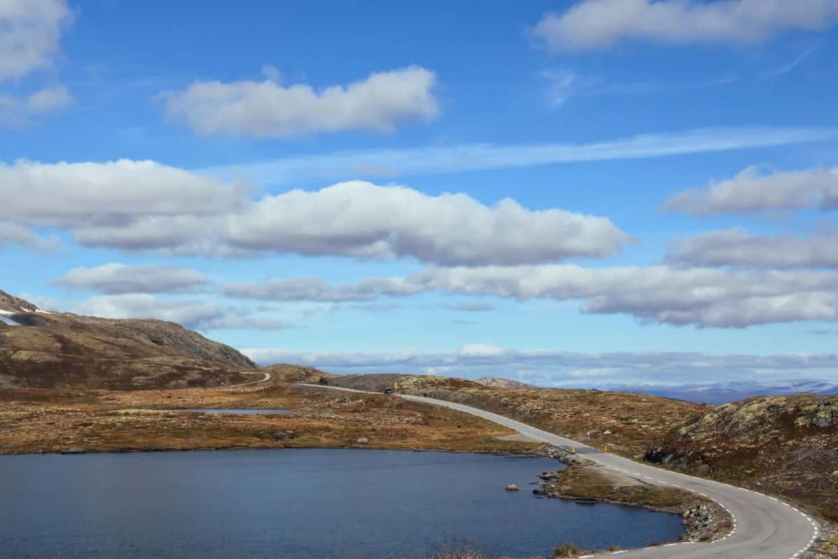 Route panoramique longeant un lac de montagne en Norvège, décor typique d'un road trip en Scandinavie