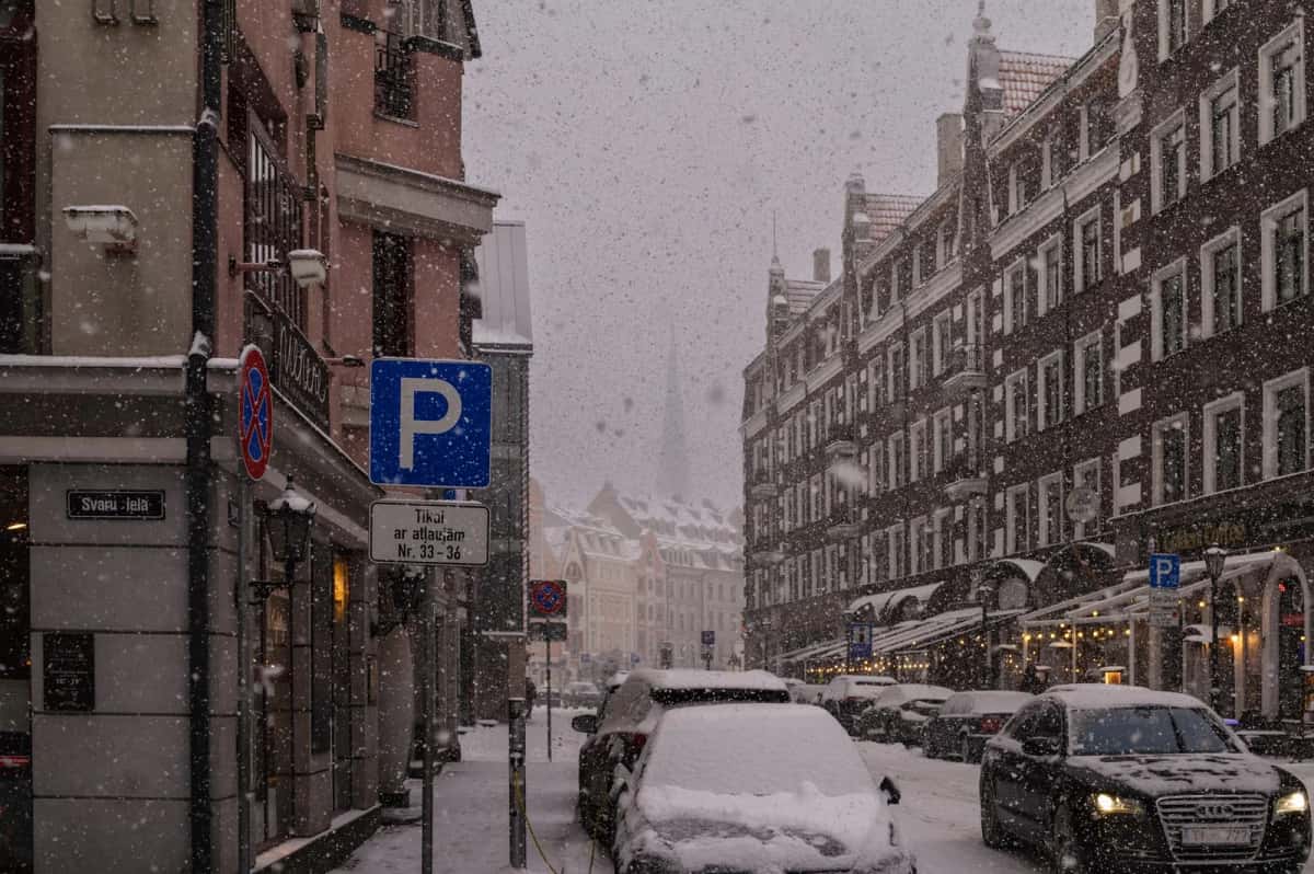 Rue de Copenhague sous une chute de neige, voitures recouvertes le long du trottoir et flèches d'églises noyées dans le gris au fond