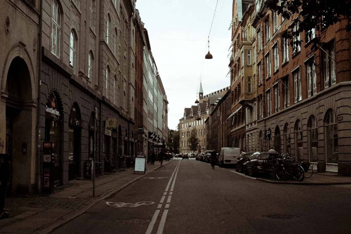 Rue en légère pente bordée d'immeubles de brique et de pierre, motos et vélos garés le long du trottoir, une flèche de cuivre vert au fond