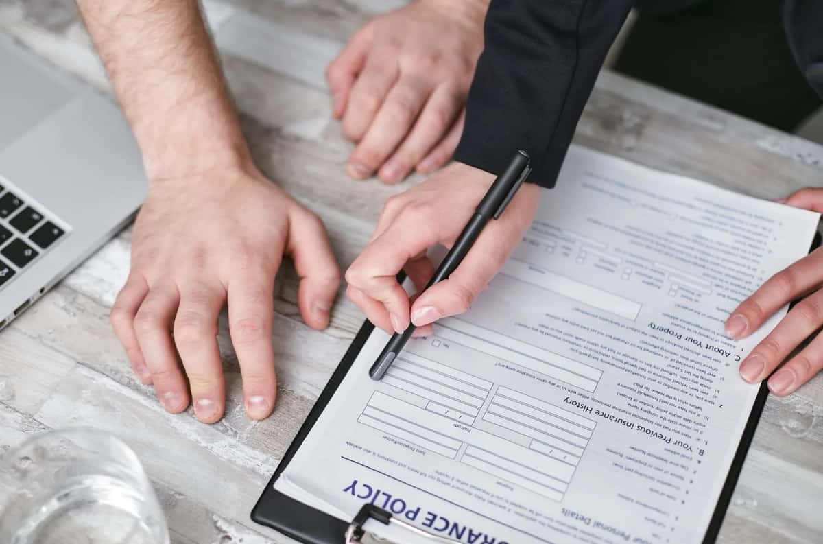 Deux personnes penchées sur un formulaire de police d'assurance, stylo en main, devant un ordinateur portable