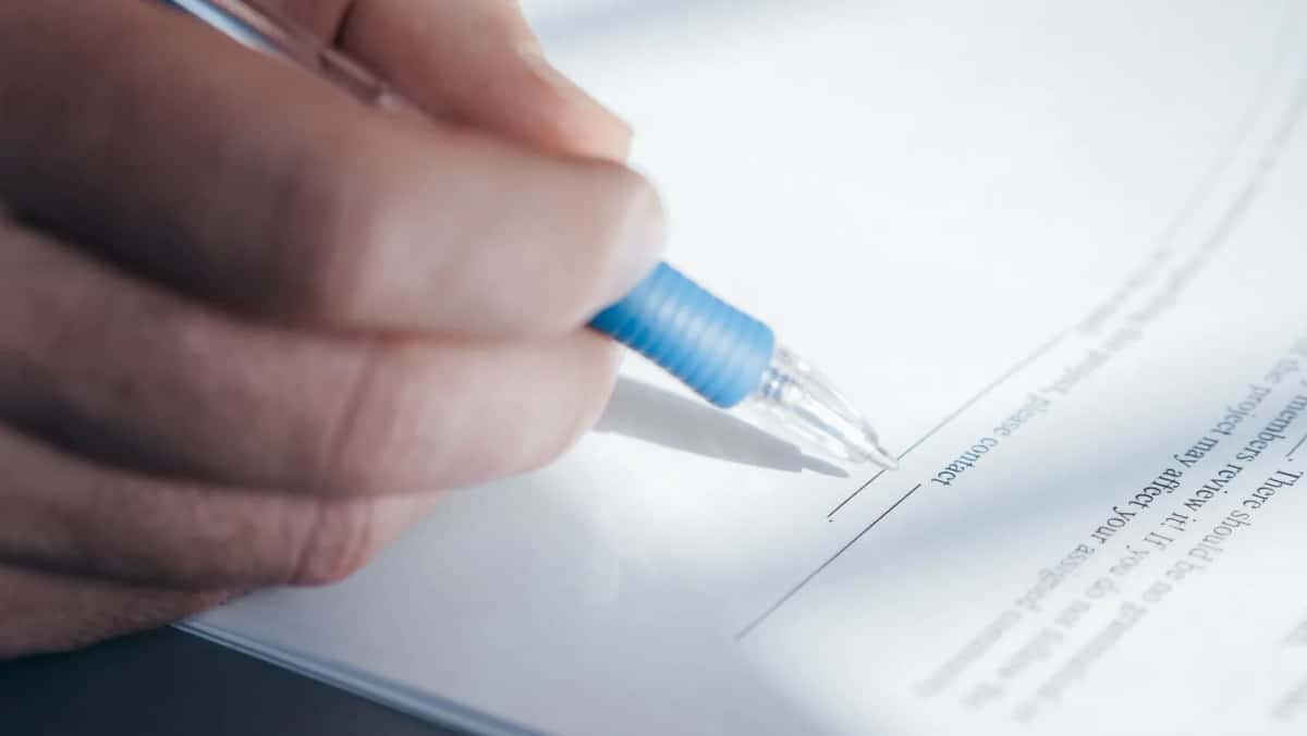 Main tenant un stylo bille au-dessus de la ligne de signature d'un document imprimé, en gros plan
