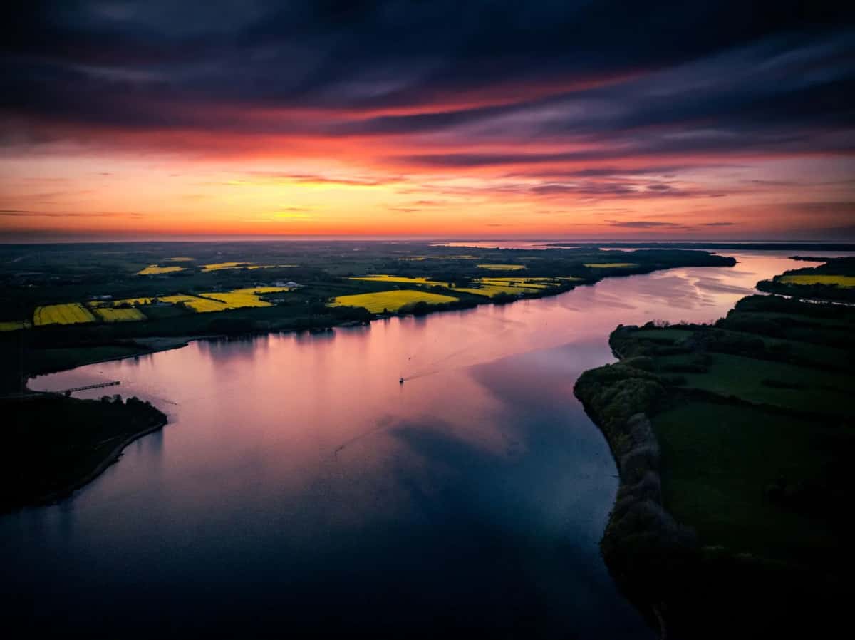 Coucher de soleil sur un bras de mer du sud du Jutland à Sønderborg, champs et bois découpés par l'eau, ciel orangé bas sur l'horizon