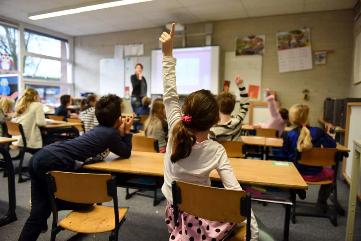 Écoliers dans une salle de classe, une élève lève la main pour participer