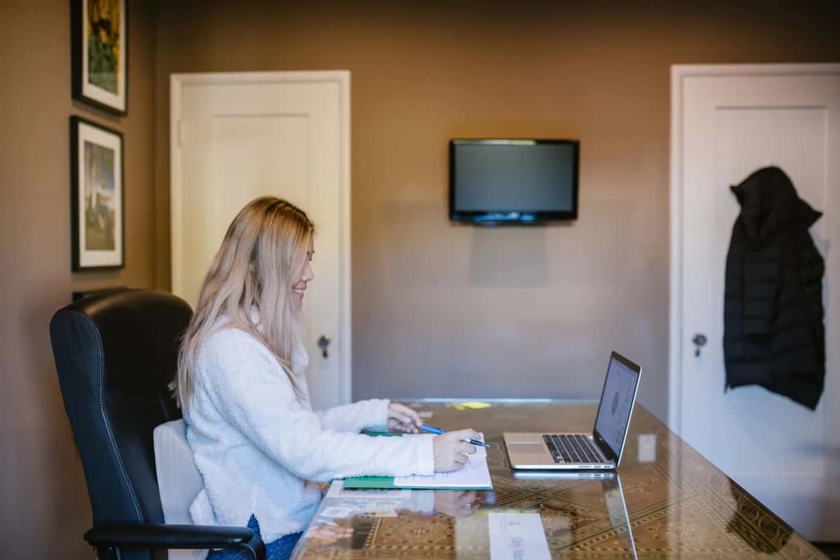Femme installée à une table devant un ordinateur portable, dans une pièce claire aménagée en bureau à domicile