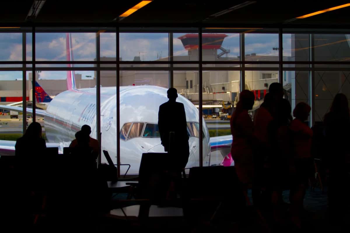 Passagers en silhouette devant la baie vitrée d'un terminal, un avion stationné au contact de l'autre côté