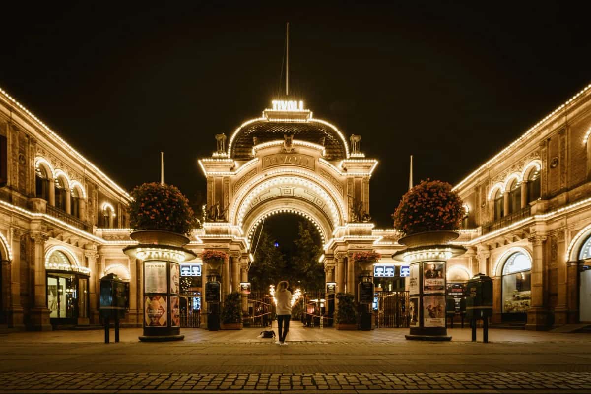 L'entrée principale de Tivoli la nuit, son arche illuminée portant l'enseigne TIVOLI, encadrée par les pavillons éclairés