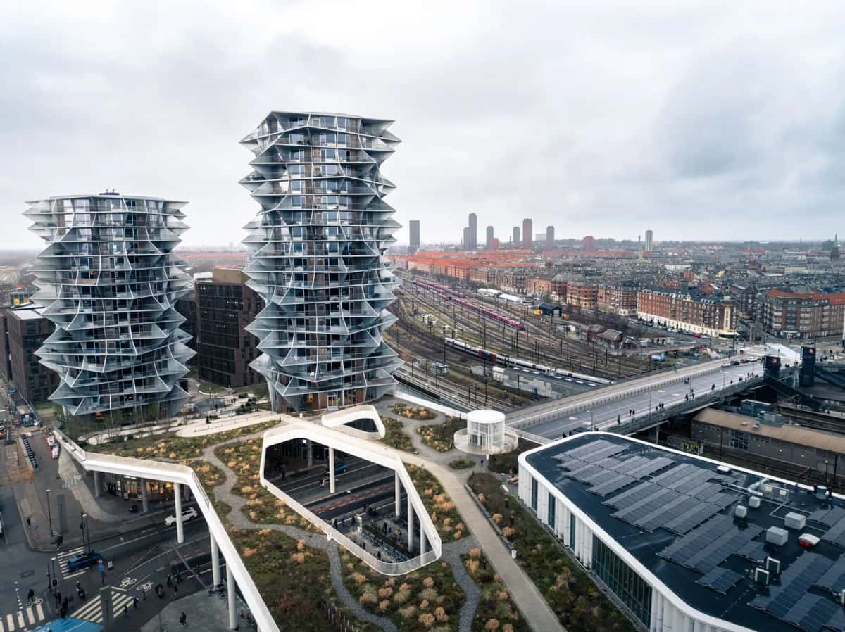 Deux tours résidentielles cylindriques aux balcons décalés en spirale, vues d'en haut, au-dessus d'un quartier neuf et de voies ferrées