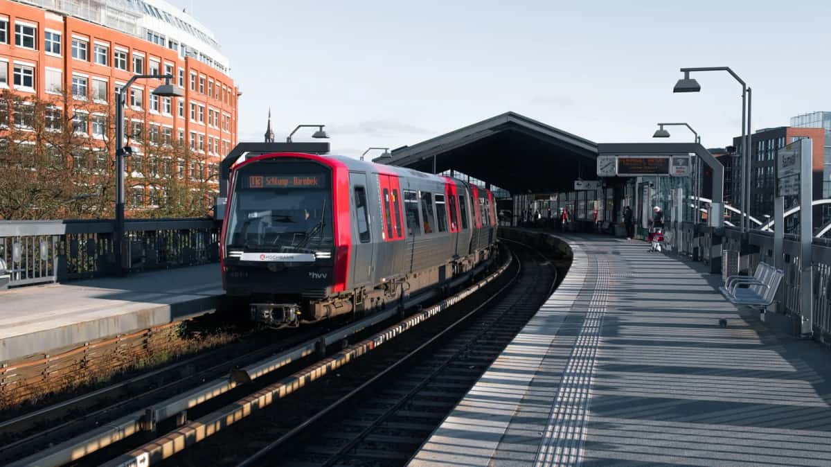 Rame de train régional à nez rouge arrêtée le long d'un quai, entre les immeubles de brique d'une ville