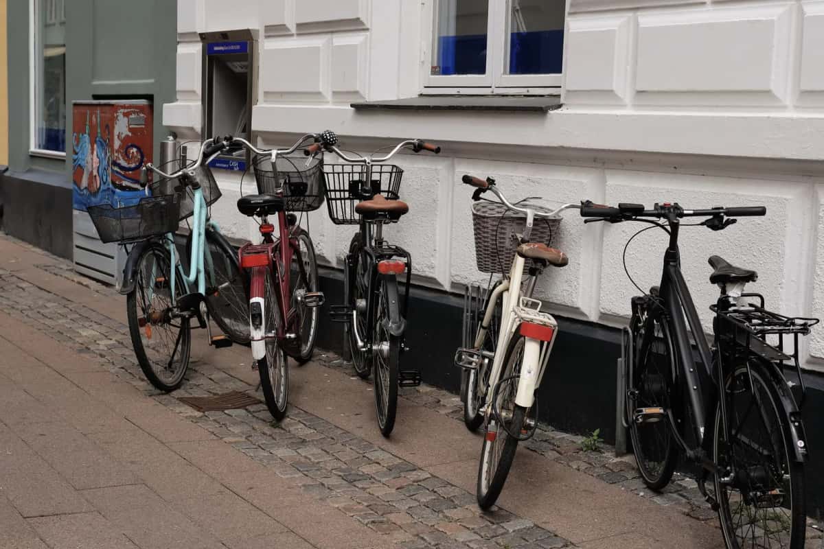 Cinq vélos appuyés contre la façade blanche d'un immeuble, le long d'un trottoir pavé