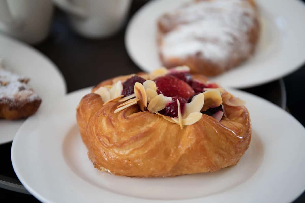 Viennoiserie danoise garnie de crème, de fruits rouges et d'amandes effilées, servie sur une assiette blanche